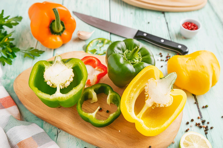 image of yellow, orange and green bell peppers on a cutting board with a knife 
